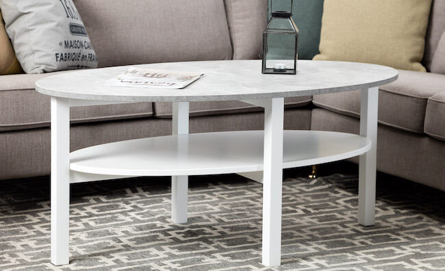 Ovalt soffbord med vita ben och en bordsskiva i betong.